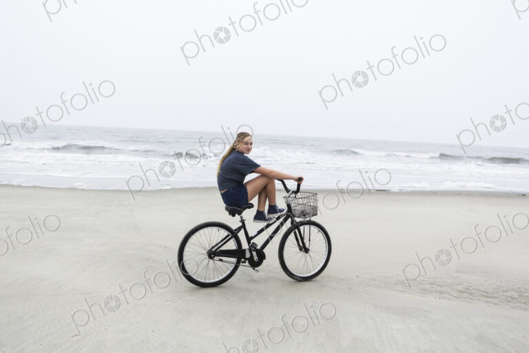 Teen girl biking on sandy beach by the ocean, St. Simon's Island, Georgia