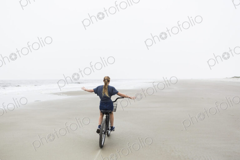 Teen girl biking on sandy beach by the ocean, St. Simon's Island, Georgia