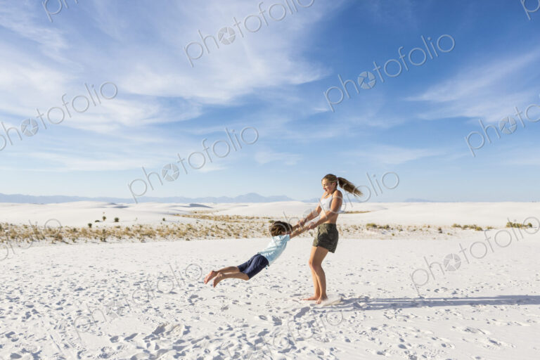 Teen girl swinging her 6 year old brother in sand, White Sands Nat'l Monument, NM
