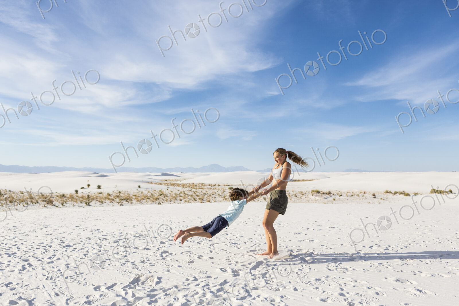 Teen girl swinging her 6 year old brother in sand, White Sands Nat’l Monument, NM