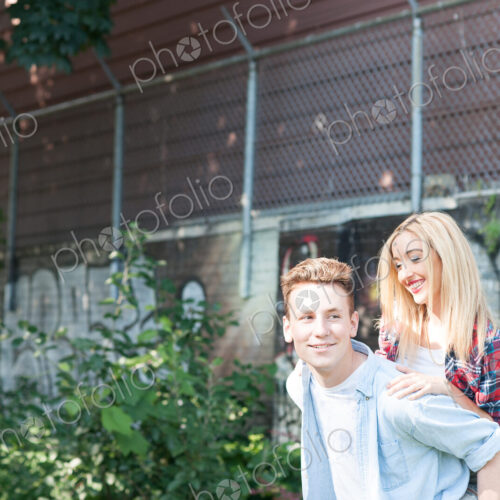 Teenage boy giving a piggy back to a boy with suburban house behind.