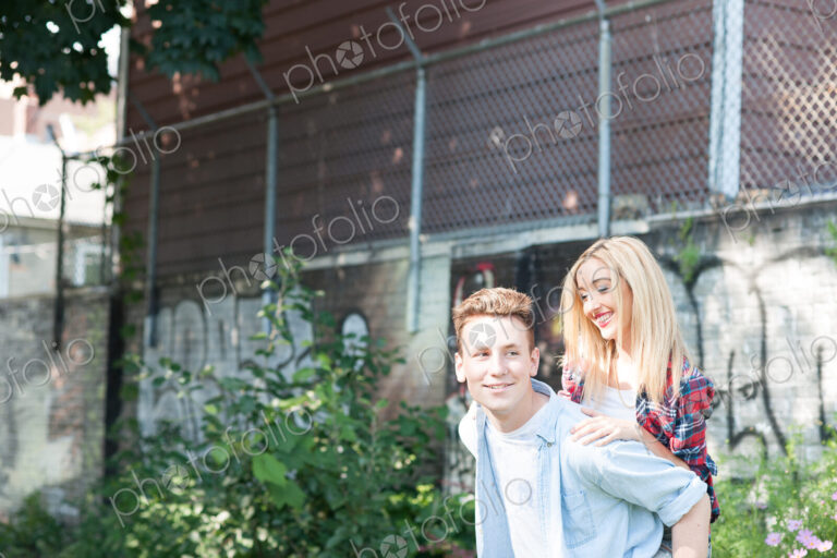 Teenage boy giving a piggy back to a boy with suburban house behind.