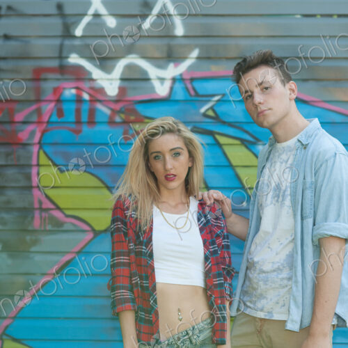 Teenage girl and boy standing in front of graffiti on wall.