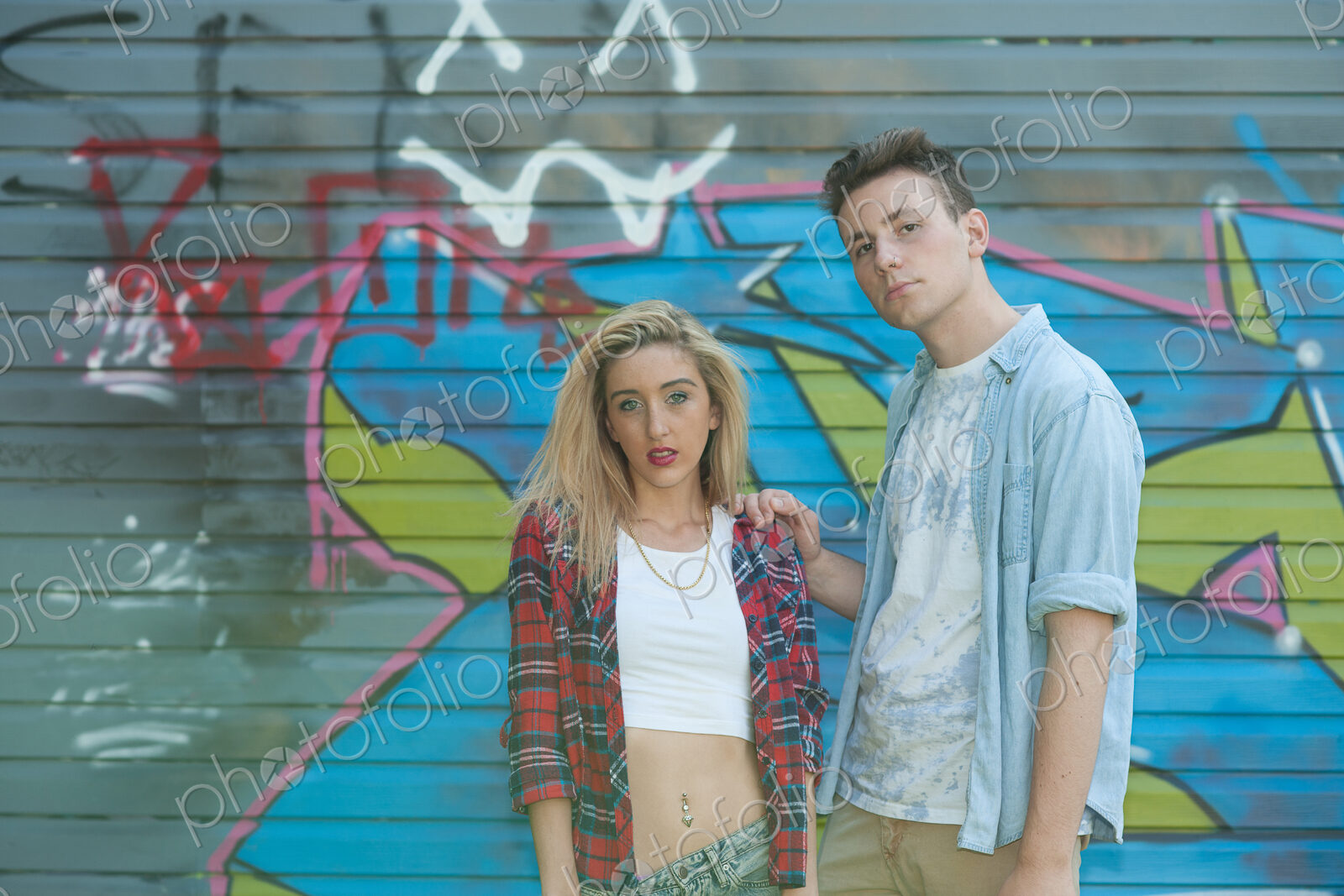 Teenage girl and boy standing in front of graffiti on wall.