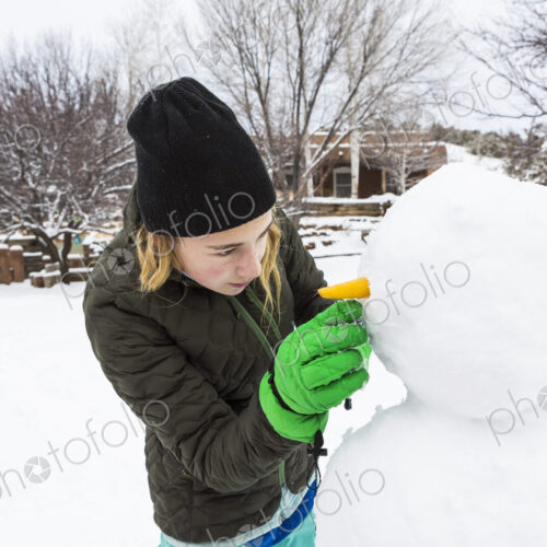 Teenage girl and her younger brother building a snowman in a garden Teenage girl and her younger brother building a snowman in a garden