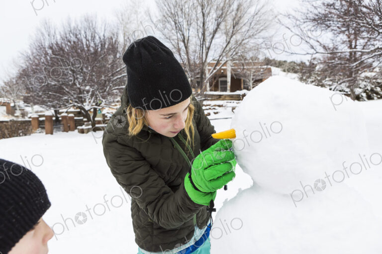Teenage girl and her younger brother building a snowman in a garden