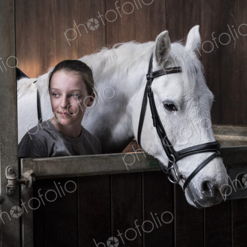 Teenage girl horserider with a grey horse outside astable, adjusting the girth and saddle.