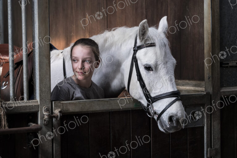 Teenage girl horserider with a grey horse outside astable, adjusting the girth and saddle.