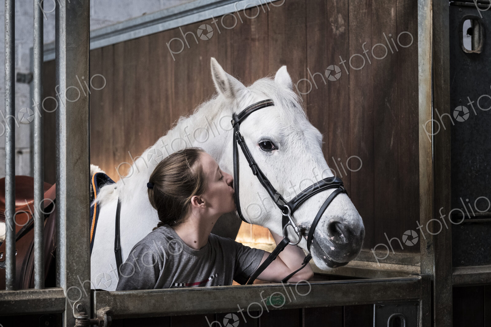 Teenage girl horserider with a grey horse outside astable, adjusting the girth and saddle.