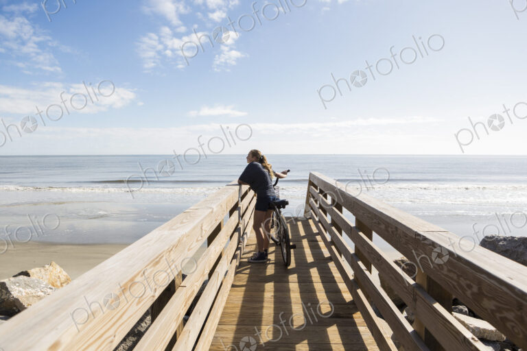 Teenage girl on wooden bridge by the beach, with her bike