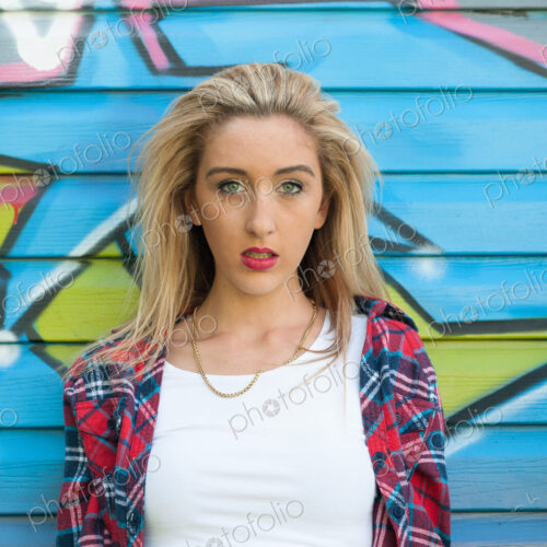 Teenage girl standing in front of graffiti on wall.
