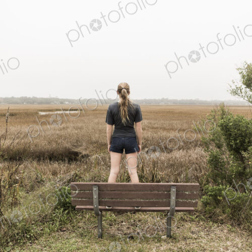 Teenage girl standing on a bench looking out over marshes, St. Simon's Island, Georgia