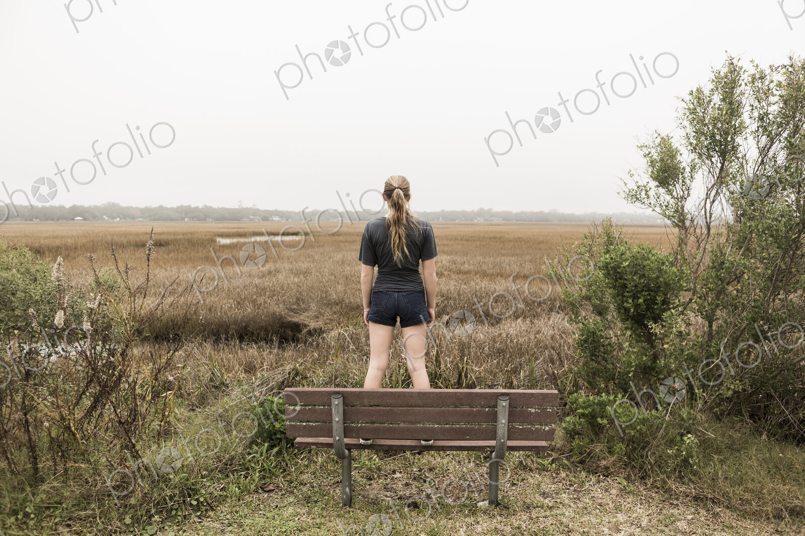 Teenage girl standing on a bench looking out over marshes, St. Simon’s Island, Georgia
