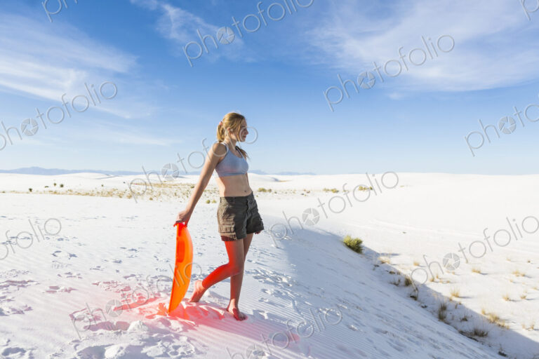 Teenage girl with a sledge at the top of a rise at White Sands Nat'l Monument, NM