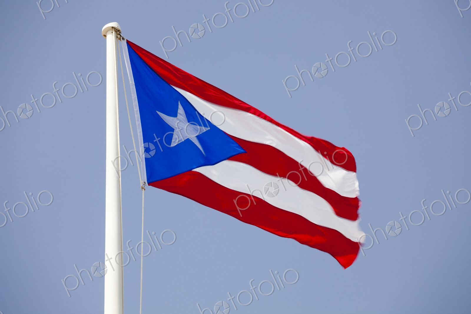 The Puerto Rican flag flutters boldly in the wind against a clear blue sky. Captured…