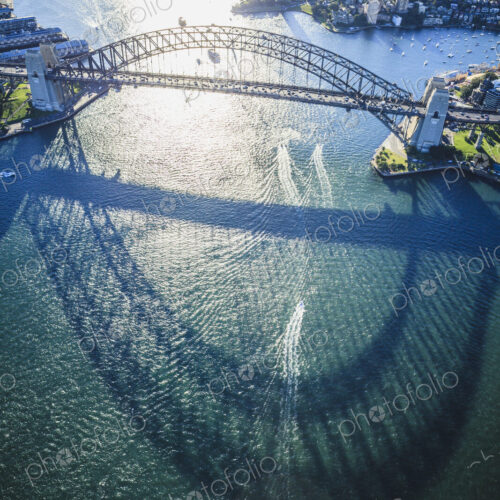 The Sydney Harbour Bridge, the shadow of the arch on the water, and aerial view of the…