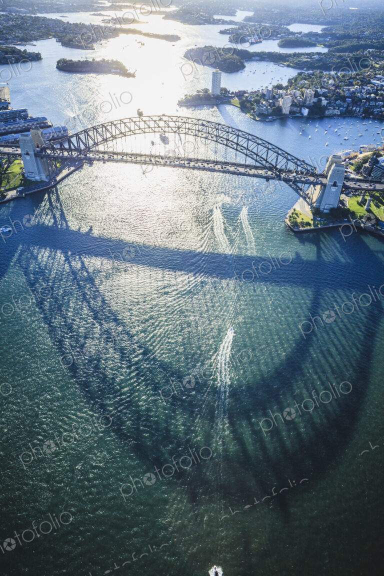 The Sydney Harbour Bridge, the shadow of the arch on the water, and aerial view of the…