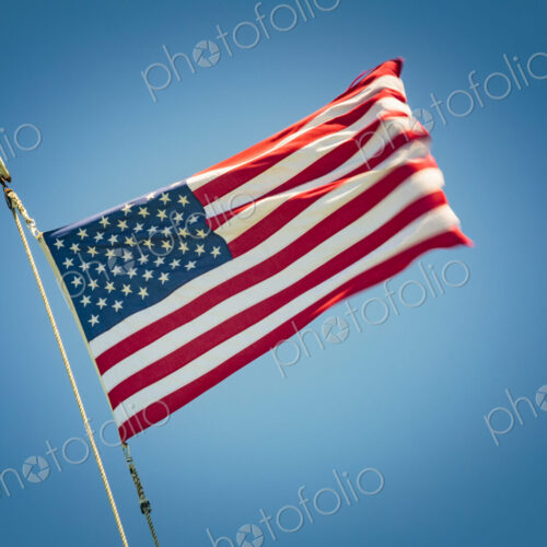 The United States flag flying against a blue sky, the stars and stripes.