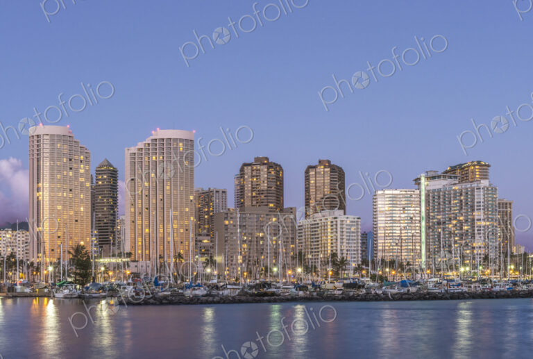 The Waikiki Skyline at dusk, tall buildings, downtown area, waterfront with moorings.