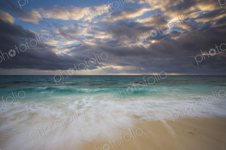 The beach and the water's edge. A cloudy sky.