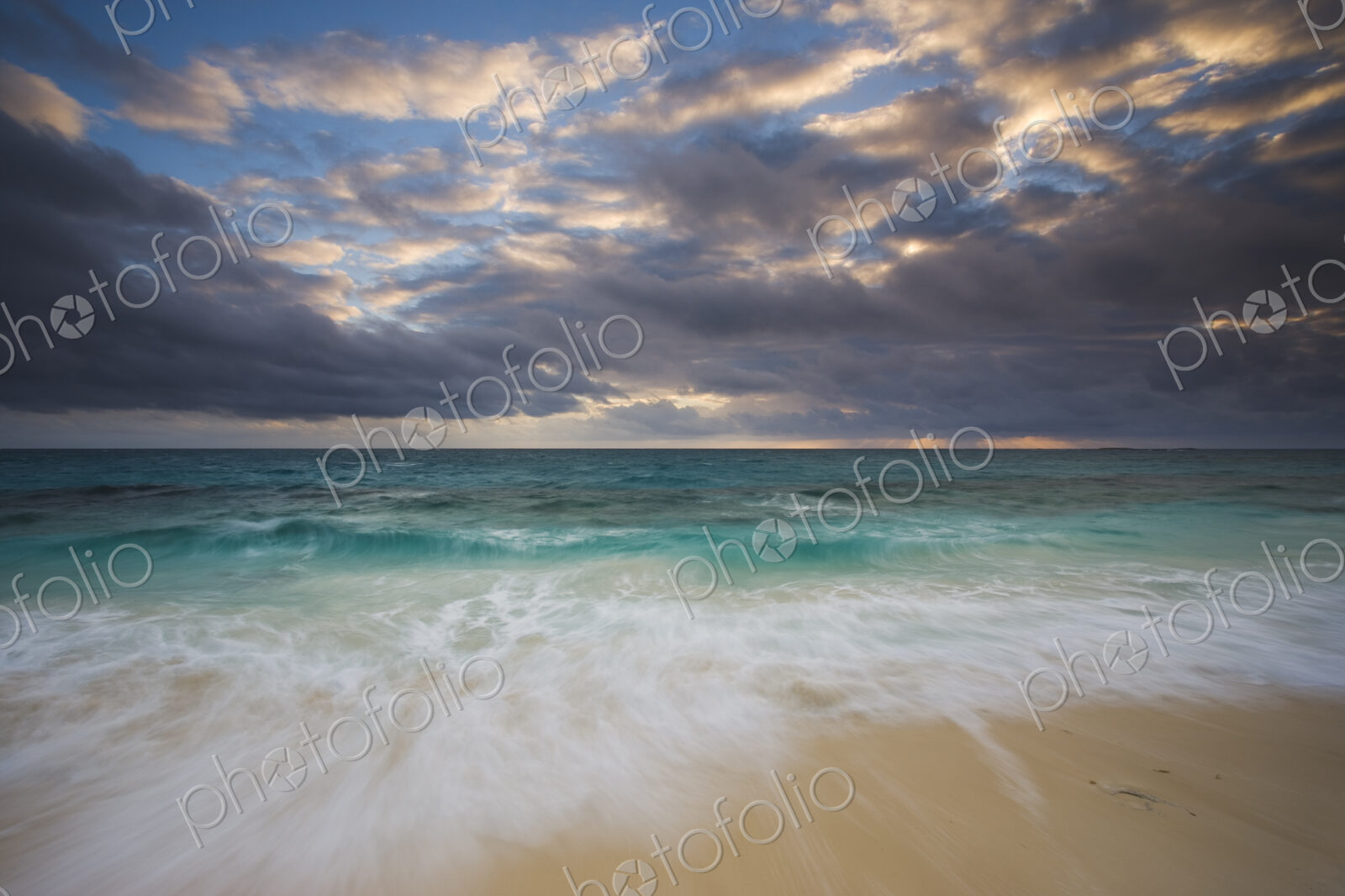 The beach and the water’s edge. A cloudy sky.