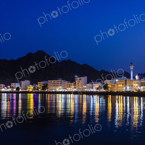 The city of Muscat, waterfront lights, mountains behind, at night