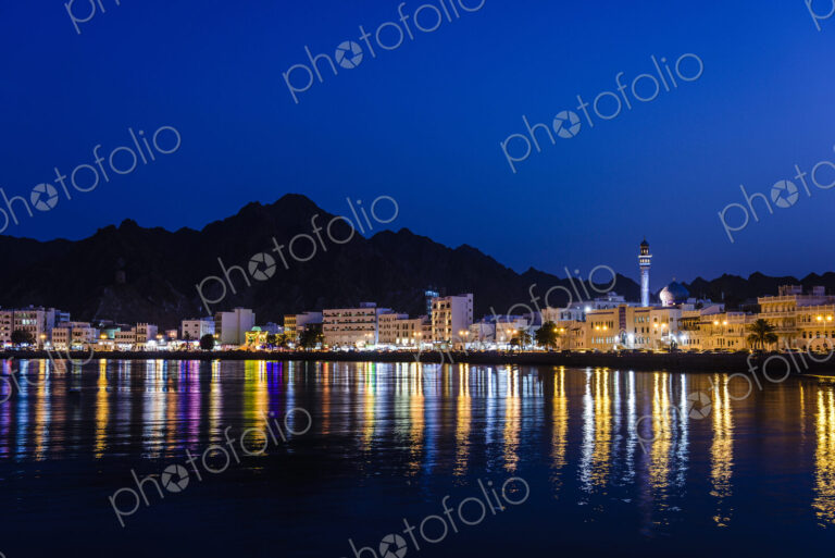 The city of Muscat, waterfront lights, mountains behind, at night