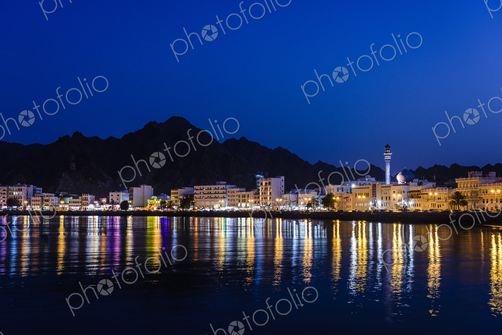 The city of Muscat, waterfront lights, mountains behind, at night