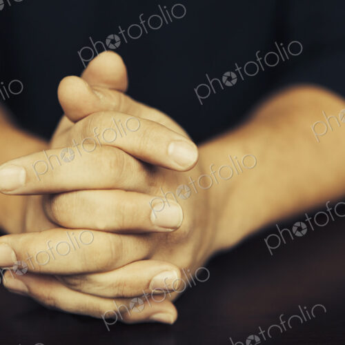 The clasped hands of a man wearing dark coloured clothes. The clasped hands of a man wearing dark coloured clothes.