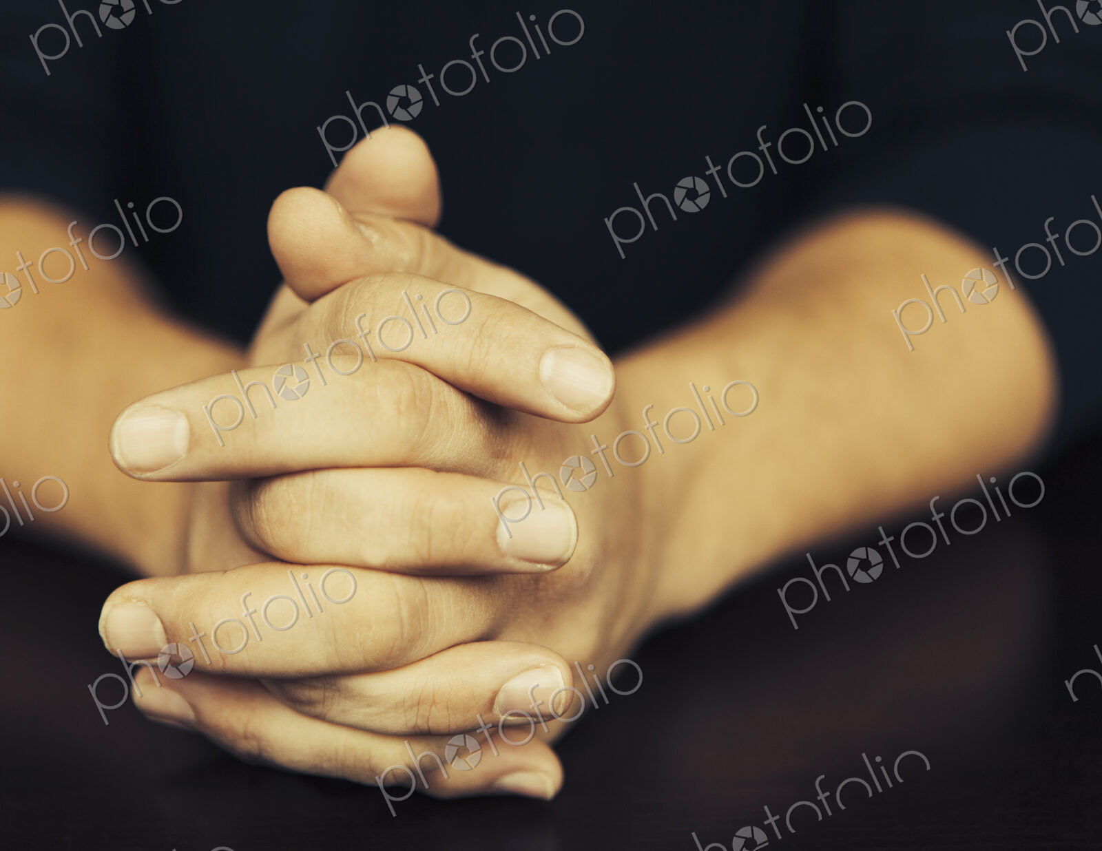 The clasped hands of a man wearing dark coloured clothes.