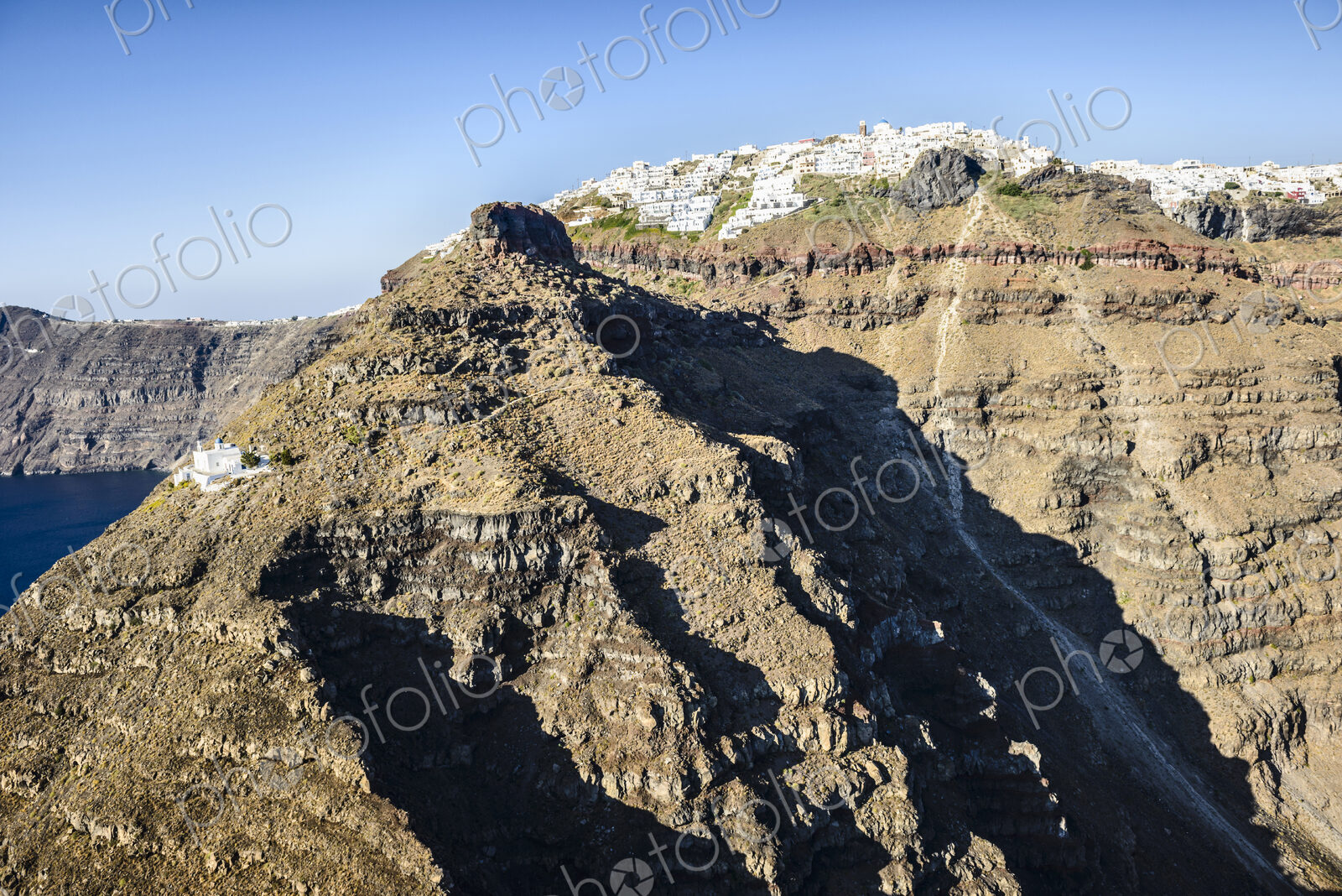 The cliffs and rock formations of an island in the Aegean sea, with a town of…