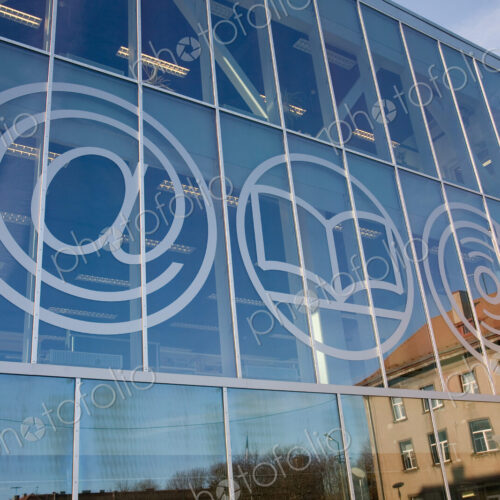 The exterior glass walls of a modern library building, internet icons etched on glass The exterior glass walls of a modern library building, internet icons etched on glass