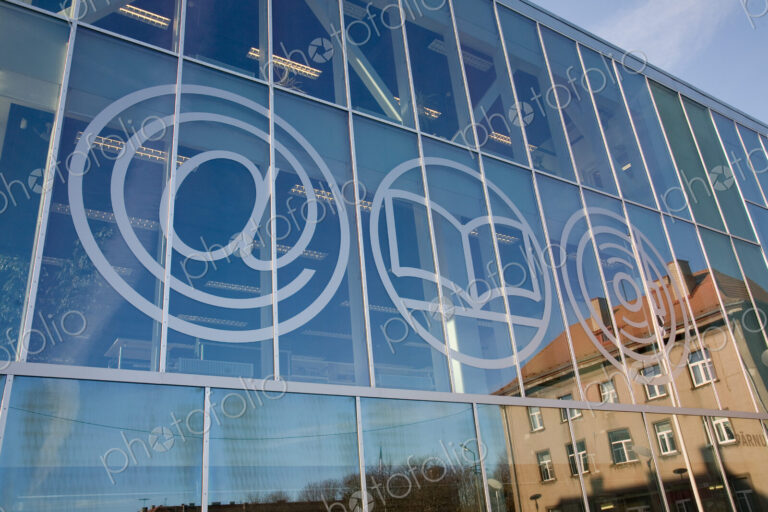 The exterior glass walls of a modern library building, internet icons etched on glass