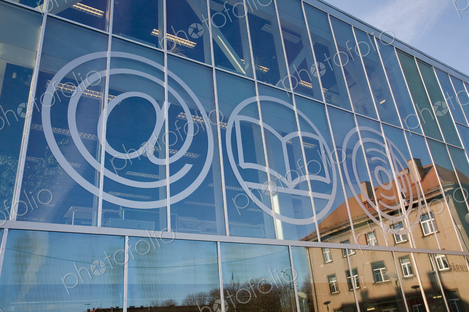 The exterior glass walls of a modern library building, internet icons etched on glass
