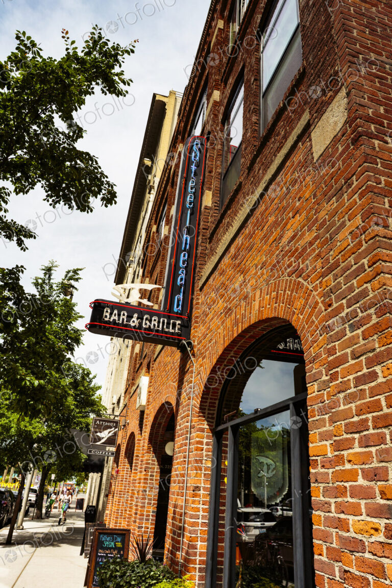The exterior of a bar, a red brick building, neon signs, and an A board advertising…