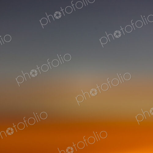 The horizon at sunset, blue sky and layers of intense orange sunlight and paler…