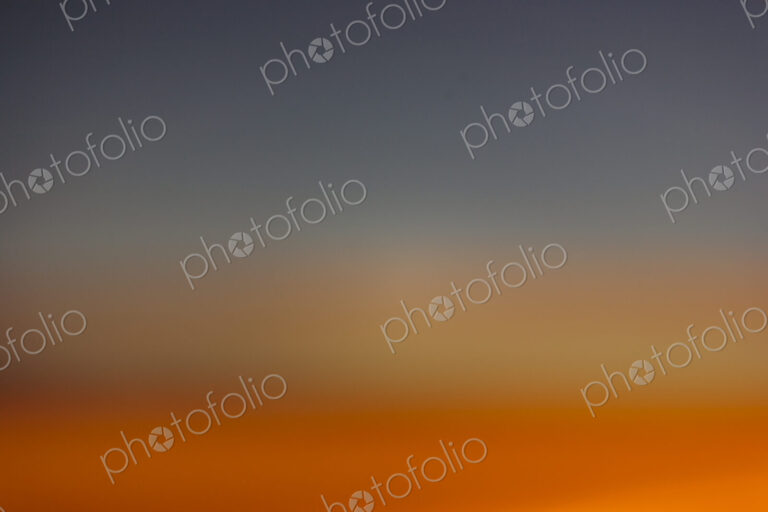 The horizon at sunset, blue sky and layers of intense orange sunlight and paler…