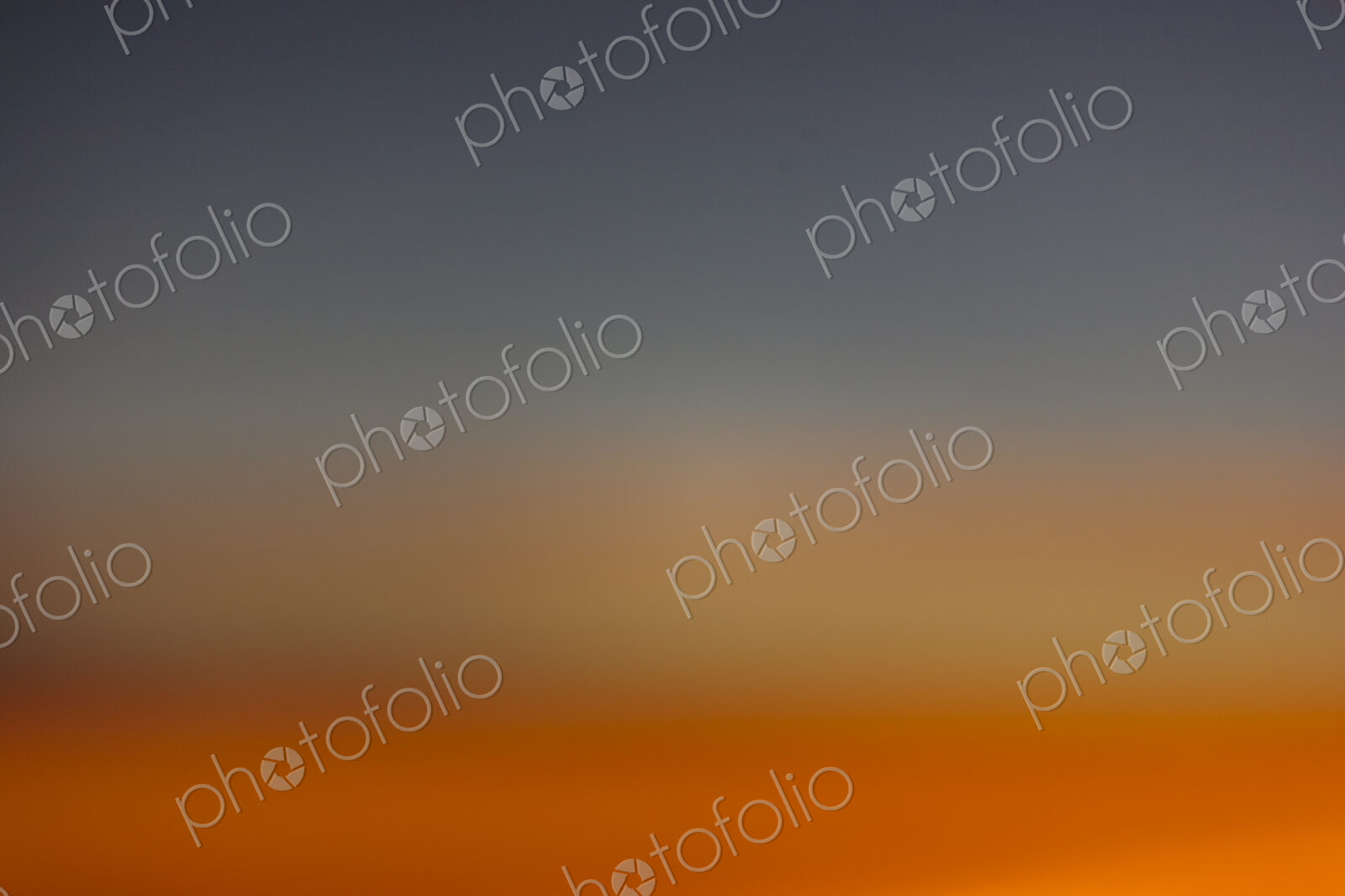 The horizon at sunset, blue sky and layers of intense orange sunlight and paler…
