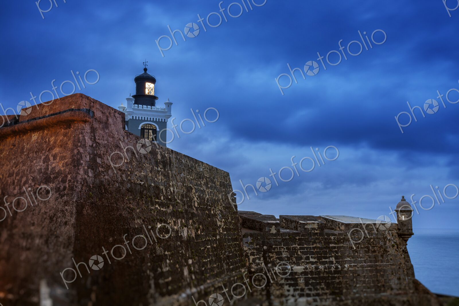 The iconic lighthouse of Castillo San Felipe del Morro glows at twilight above the…