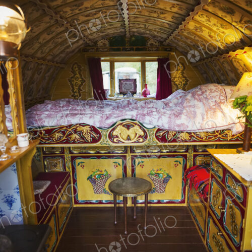 The interior of a traditional gypsy caravan with raised bed and cupboards, bow top…