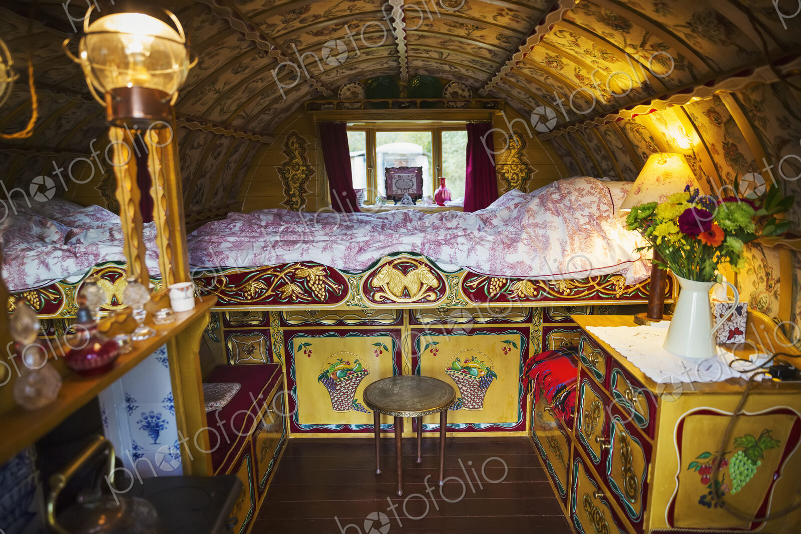 The interior of a traditional gypsy caravan with raised bed and cupboards, bow top…