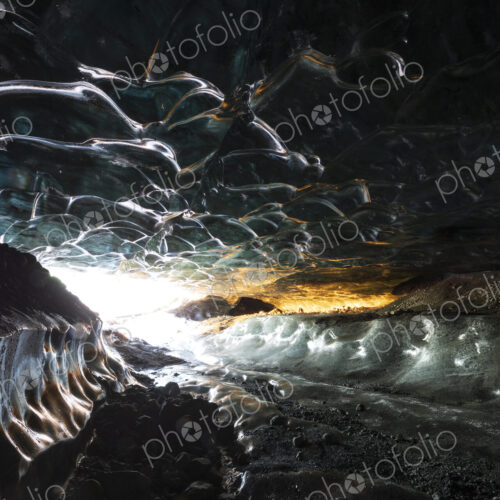 The interior of an ice cave with clear contoured ice on the ceiling, walls of ice and…
