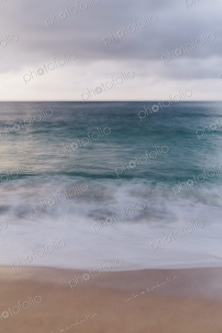 The ocean viewed from the beach, waves breaking on the beach and overcast sky.