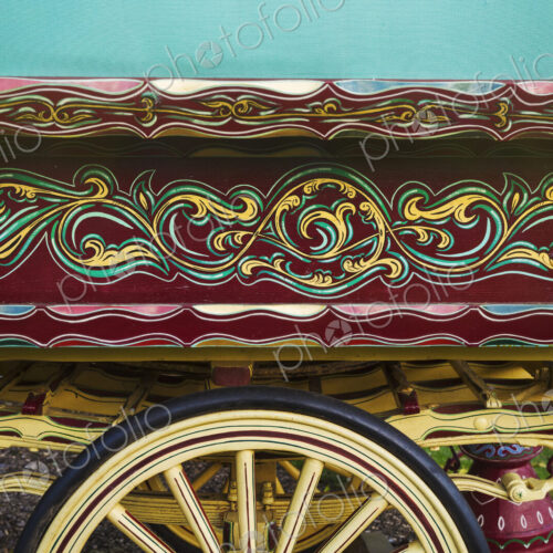 The painted decorated side panel of a bow top gypsy caravan and large wooden wheel.