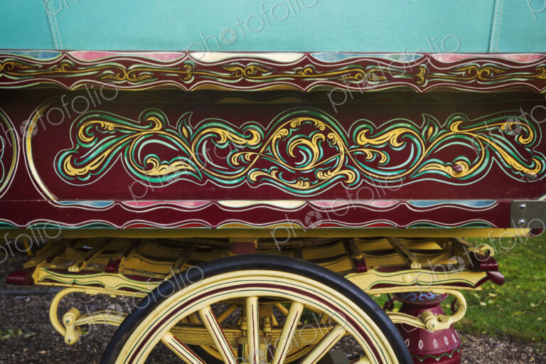 The painted decorated side panel of a bow top gypsy caravan and large wooden wheel.
