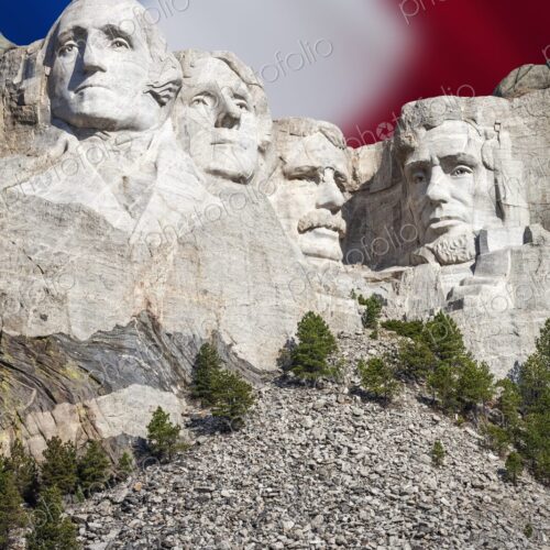 The presidential carvings of Mount Rushmore stand before a soft focus American flag in… The presidential carvings of Mount Rushmore stand before a soft focus American flag in…