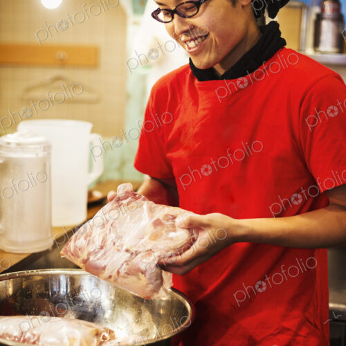 The ramen noodle shop. A chef preparing a huge metal bowl of broth with meat ingredients.