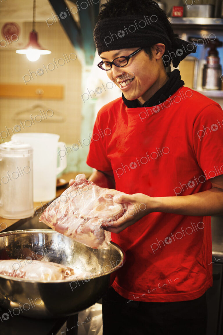 The ramen noodle shop. A chef preparing a huge metal bowl of broth with meat ingredients.