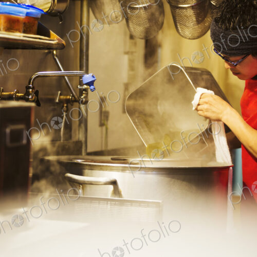 The ramen noodle shop. A chef working in a kitchen preparing food using a stove and…