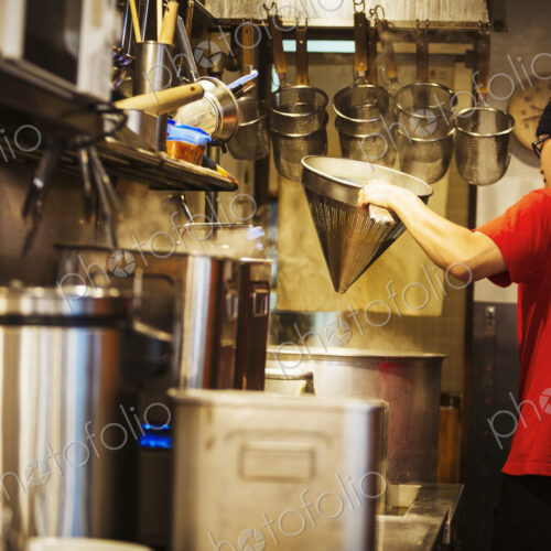 The ramen noodle shop. A chef working in a kitchen preparing food using a stove and…